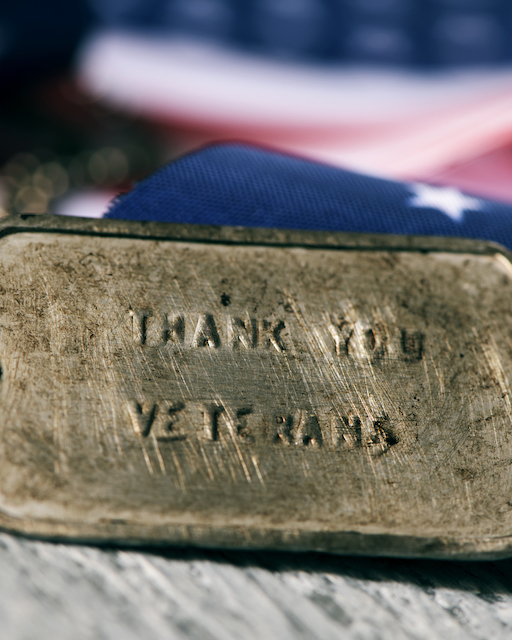 Closeup,Of,A,Rusty,Dog,Tag,With,The,Text,Thank closeup of a rusty dog tag with the text thank you veterans engraved in it, next to a flag of the United States, on a rustic wooden surface
